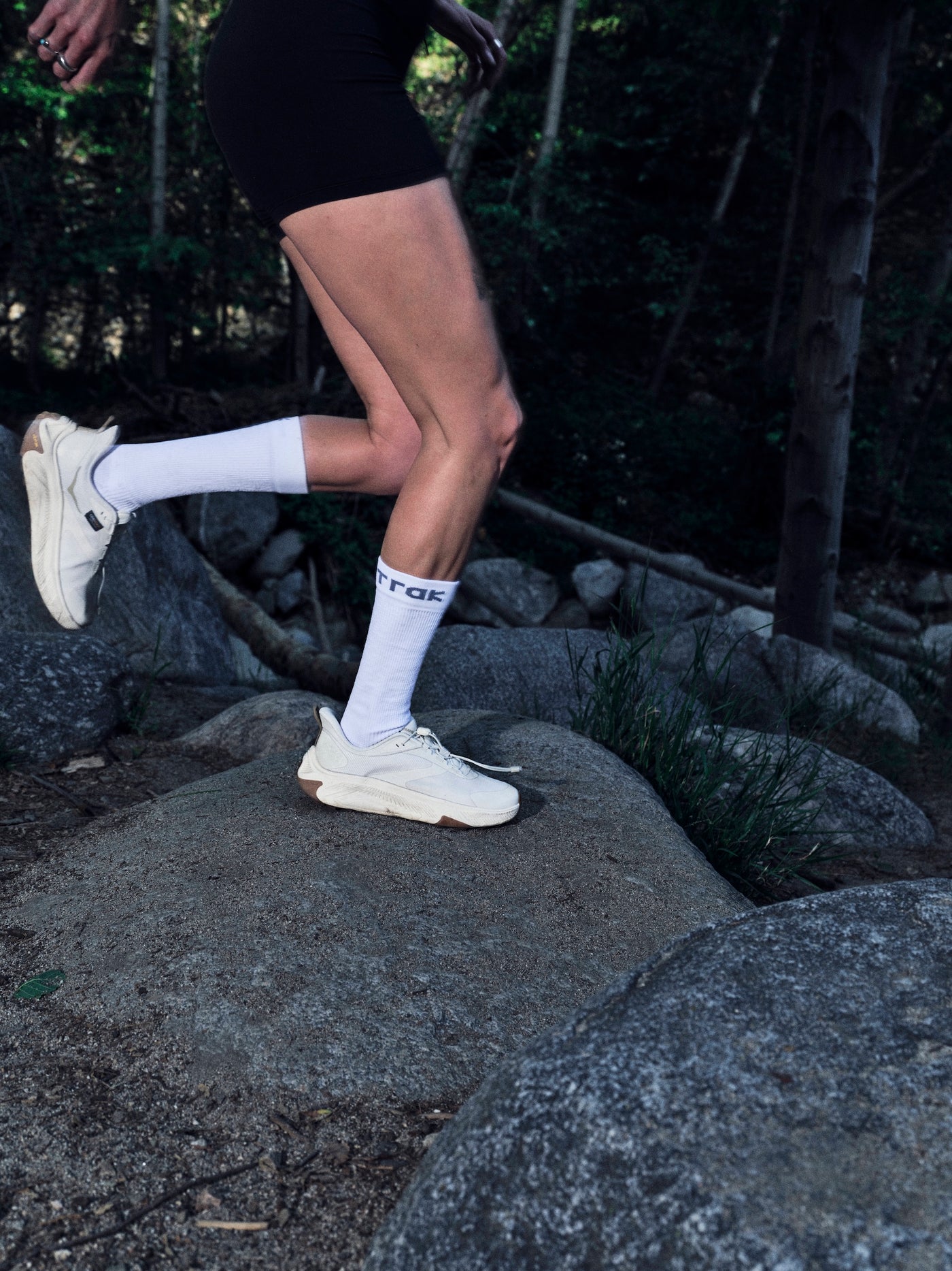 Person running on rocks with white sneakers and socks in a forest setting